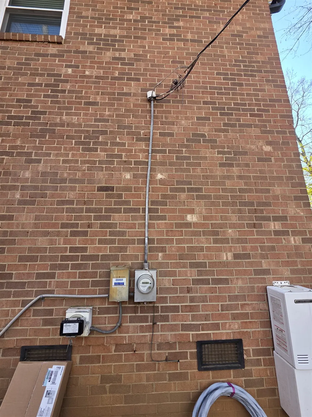 Existing overhead electrical service before replacement on a brick building